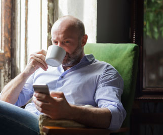 man sipping coffee looking up body corporate manager on mobile pgone